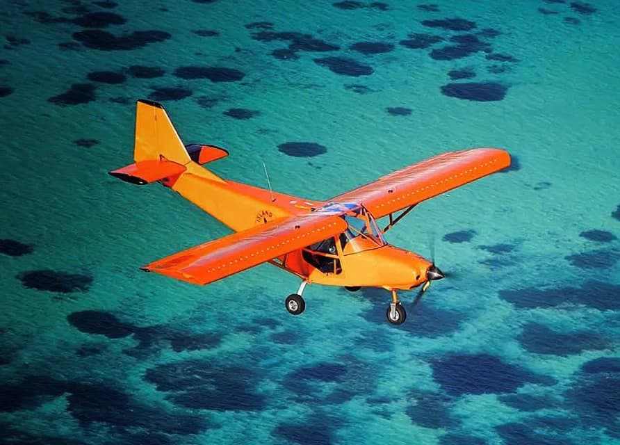 An orange Savannah microlight over the turquoise lagoon