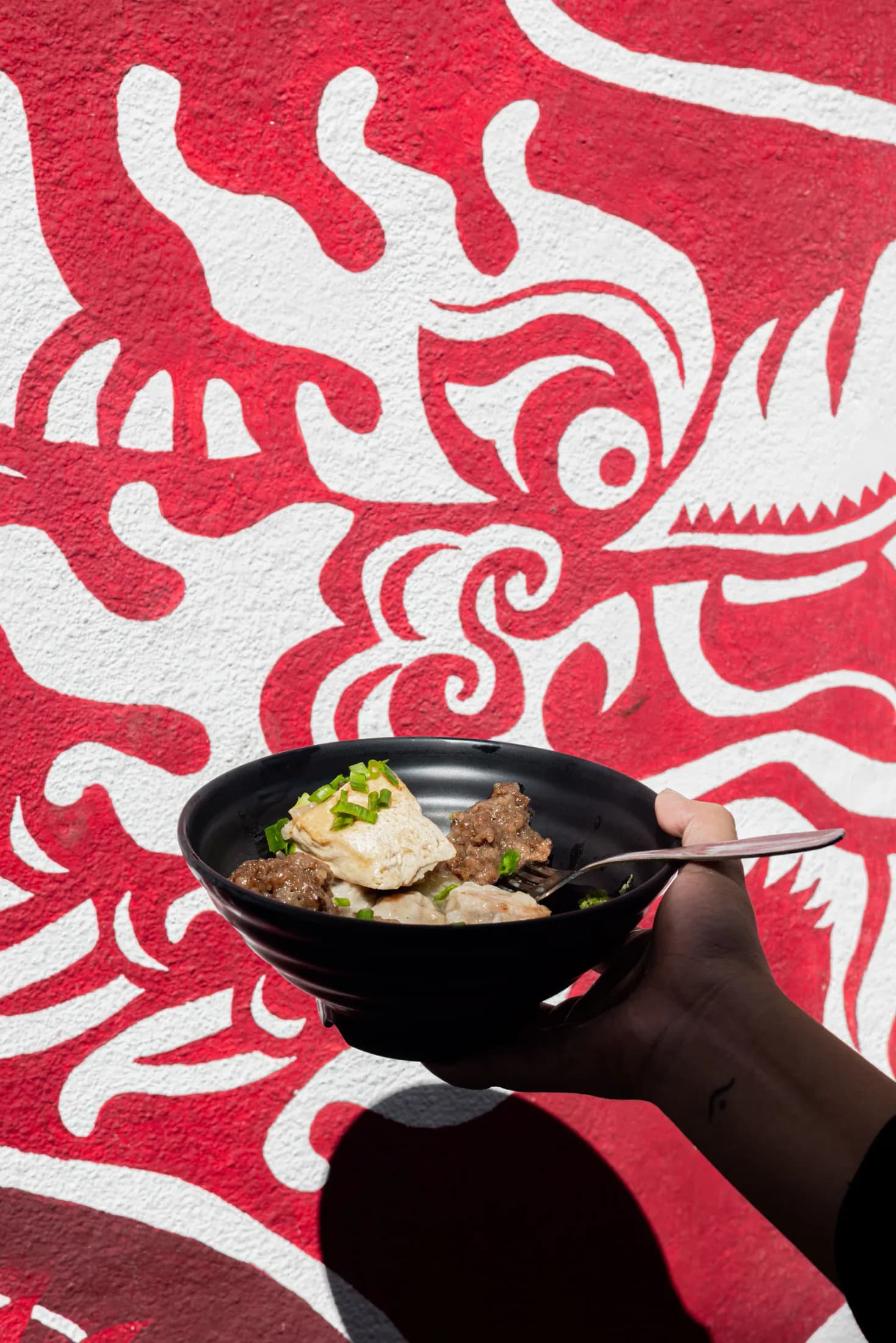 Bowl of Mauritian street food against a red and white mural in Port Louis